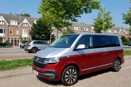 Dwukolorowy volkswagen van, czerwono-srebrny, zaparkowany na tle domów i drzew.