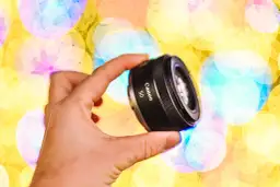 Dłoń trzyma obiektyw Canon 50mm na tle kolorowych świateł bokeh.
