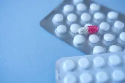 Dwie blistry białych tabletek, jedna z nich zawiera kapsułkę z różowymi granulkami, przypominającą clonazepam.