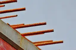 Zardzewiałe pręty zbrojeniowe wystające z betonowej formy na tle jasnego nieba.