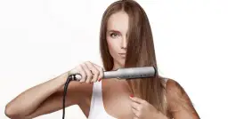 Kobieta prostuje długie, brązowe włosy prostownicą na białym tle.