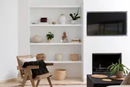 Elegancka aranżacja półki w salonie z ceramiką, roślinami i figurką Buddy. Obok wygodny fotel i kominek.