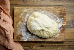Surowe ciasto na pizzę na desce, posypane mąką. Zastanawiasz się, czy ciasto na pizzę można zamrozić? Tak, można!