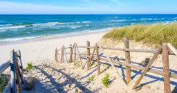 Piękna plaża w Łebie, idealne miejsce na spacer. Drewniane płotki prowadzą do morza, a trawy na wydmach dodają uroku.