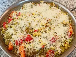 Arroz a la milanesa listo para hornear, cubierto con queso rallado y vegetales frescos como tomates, zanahorias y guisantes.