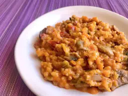 Un cremoso risotto de calabaza con trozos de champiñones y pimientos, servido en un plato blanco sobre un mantel morado.