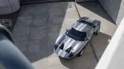 Srebrny Ford GT40 z białymi pasami, gotowy do wyścigu. Ikona motoryzacji na betonowym placu.