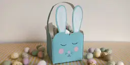 Uroczy, niebieski koszyczek z kartonu w kształcie królika, wypełniony wielkanocnymi jajeczkami. Idealny pomysł, jak zrobić koszyk z kartonu na święta.