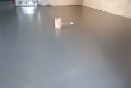 Świeżo wylany, gładki **pianobeton** na podłodze. W tle widać wiaderko i instalacje.