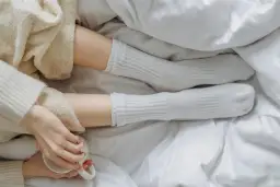 Piernas con calcetines blancos de poliamida, envueltas en mantas suaves, sosteniendo una taza.