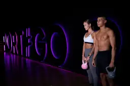 Para dwojga z kettlebellami na tle neonowego napisu "PORT#GO".