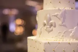 Elegancki tort weselny z ozdobami z masy cukrowej, jak przykleić ozdoby z masy cukrowej do tortu? Delikatne lilie i ptaszki zdobią białe warstwy.