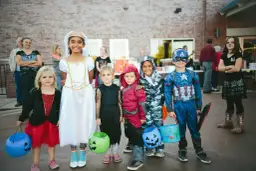 Dzieci w strojach na Halloween, gotowe na psikusy i zbieranie słodyczy. Wśród nich księżniczka, Kapitan Ameryka i inne postacie.