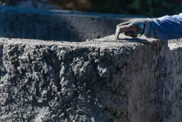 Ręka w rękawicy wygładza świeży beton. Zastanawiasz się, ile kosztuje worek cementu do takiej pracy?