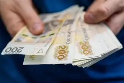 Dłonie trzymają plik banknotów 200 zł. Zastanawiasz się, ile wynosi zasiłek dla bezrobotnych?