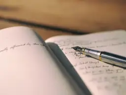 Eleganckie pióro leży na otwartym notatniku, gdzie widać ręcznie pisany tekst, między innymi skrót.