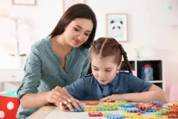 Terapeuta pomaga dziecku z niepełnosprawnością intelektualną w stopniu lekkim układać kolorowe puzzle.