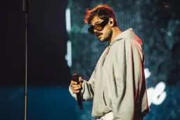Taco Hemingway w okularach i szarej bluzie z kapturem, trzymający mikrofon. Fani czekają na koncert Taco Hemingway 2026.