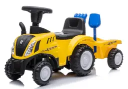 Żółty traktor New Holland z przyczepą, zabawka dla małego rolnika. Ma czarne siedzenie, kierownicę i niebieską łopatkę.