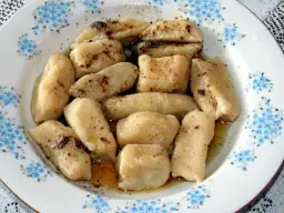 Gotowe pierogi leniwe, polane masłem i posypane cynamonem, czekają na talerzu z niebieskimi kwiatuszkami.