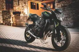Czarny motocykl Kawasaki na brukowanej ulicy, z budynkami w tle.
