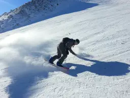 Snowboardzista w akcji na stoku, tworząc obłok śniegu. Idealne **deski do freeride** pozwalają na takie ewolucje.