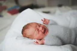 Malutkie 1,5 roczne dziecko rzuca się w nocy, ubrany w szary sweterek, leży na białej pościeli.