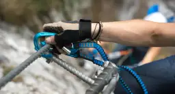 Ręka w rękawiczce z karabinkiem i lonżą, kluczowy element via ferrata sprzętu, zabezpiecza wspinaczkę.