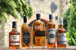 Jak odczytać etykietę szkockiej whisky: Islay, Highlands, Speyside. Pięć butelek whisky na drewnianym stole.