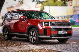 Czerwony Hyundai Santa Fe 2025 z charakterystycznym przednim grillem i światłami, zaparkowany na brukowanej ulicy.
