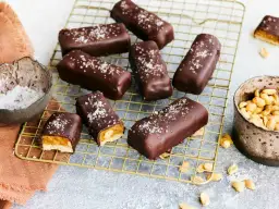 Vegane Snickers mit Karamell, Erdnüssen und Meersalz bestreut, auf einem goldenen Gitter.