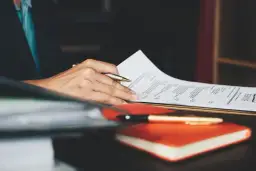 Ręka trzymająca długopis nad dokumentem z napisem "RESUME". To idealny moment na dopracowanie swojego CV po angielsku.