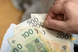 Dłoń trzyma plik banknotów 100 i 200 zł, symbolizujący nową płacę minimalną.