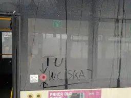 Brudne drzwi pociągu z napisem "TU WCISKAJ" i ikoną przycisku otwierania drzwi.