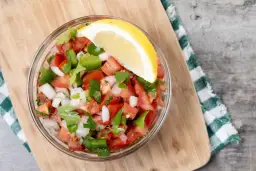 Un tazón de pico de gallo fresco, con tomate, cebolla, pimiento verde y cilantro, adornado con una rodaja de limón.