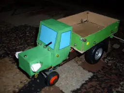 Zielony traktor z kartonu, z niebieskimi szybami i drewnianą skrzynią. Oto jak zrobić taki traktor z kartonu!