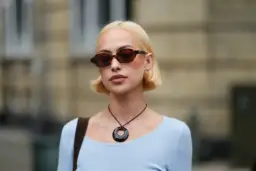 Krótkie fryzury bob w blondzie, stylowe okulary i naszyjnik z okrągłą zawieszką.