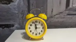 Żółty budzik z dzwonkami, który może oznaczać zakłócanie ciszy nocnej.