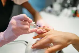 Stylistka w różowych rękawiczkach pokazuje, jak nakładać żel budujący na paznokieć.