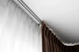 Elegancki karnisz mocowany do sufitu, z białymi i brązowymi zasłonami, tworzy przytulną atmosferę.
