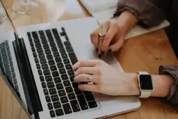 Dłonie piszące na klawiaturze laptopa, z widocznym zegarkiem i pierścionkami.