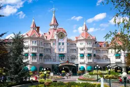 Grand hôtel rose de style victorien avec des tours, un grand cadran d'horloge et des jardins fleuris.