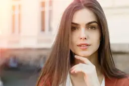 Portret młodej kobiety z dłonią pod brodą, w tle budynek.