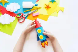 Dziecko tworzy rakietę z kartonu, używając kolorowego papieru, nożyczek i kleju. To świetny sposób, jak zrobić rakietę z kartonu!