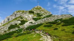 Tłum turystów podąża kamienistą trasą na Giewont. W oddali widać szczyt z krzyżem.