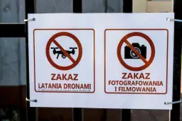 Dwa znaki na płocie: zakaz latania dronami i zakaz fotografowania i filmowania.