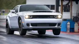 Srebrny Dodge Challenger SRT na torze wyścigowym, z przednimi kołami lekko uniesionymi nad asfaltem.