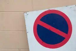 Znak zakazu postoju na tle beżowej ściany.