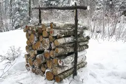 Stos drewna opałowego w śniegu, podtrzymywany przez drewniane podpory.