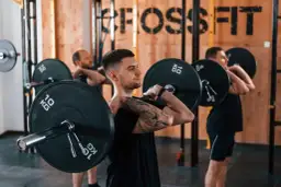 Trzech mężczyzn w siłowni CrossFit wykonuje ćwiczenia ze sztangą na klatce piersiowej.